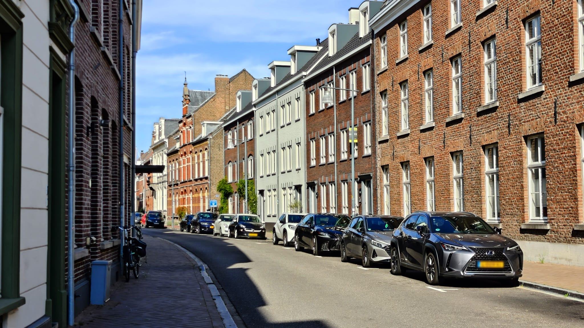 Straat met bakstenen herenhuizen en een rij geparkeerde auto's langs de stoep