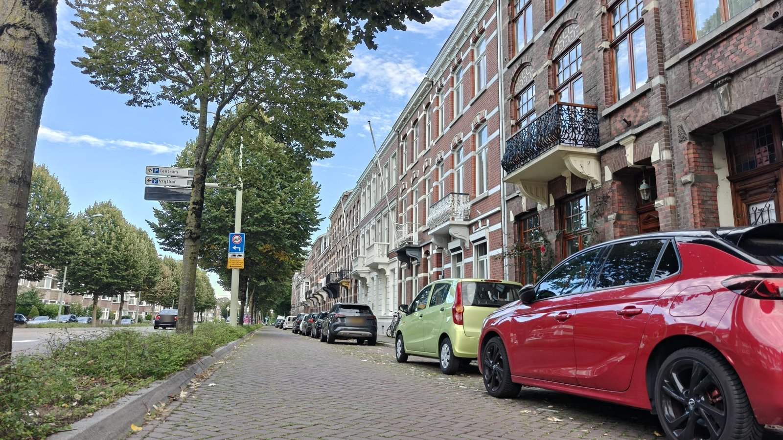 Geparkeerde auto's langs een rij herenhuizen in Maastricht, met borden naar de parkeergarages Centrum en Vrijthof