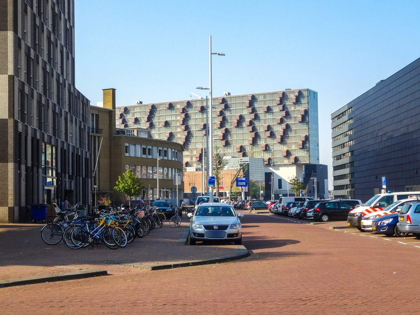 Stadsstraat met een geparkeerde taxi, fietsenrekken en moderne kantoor- en woongebouwen