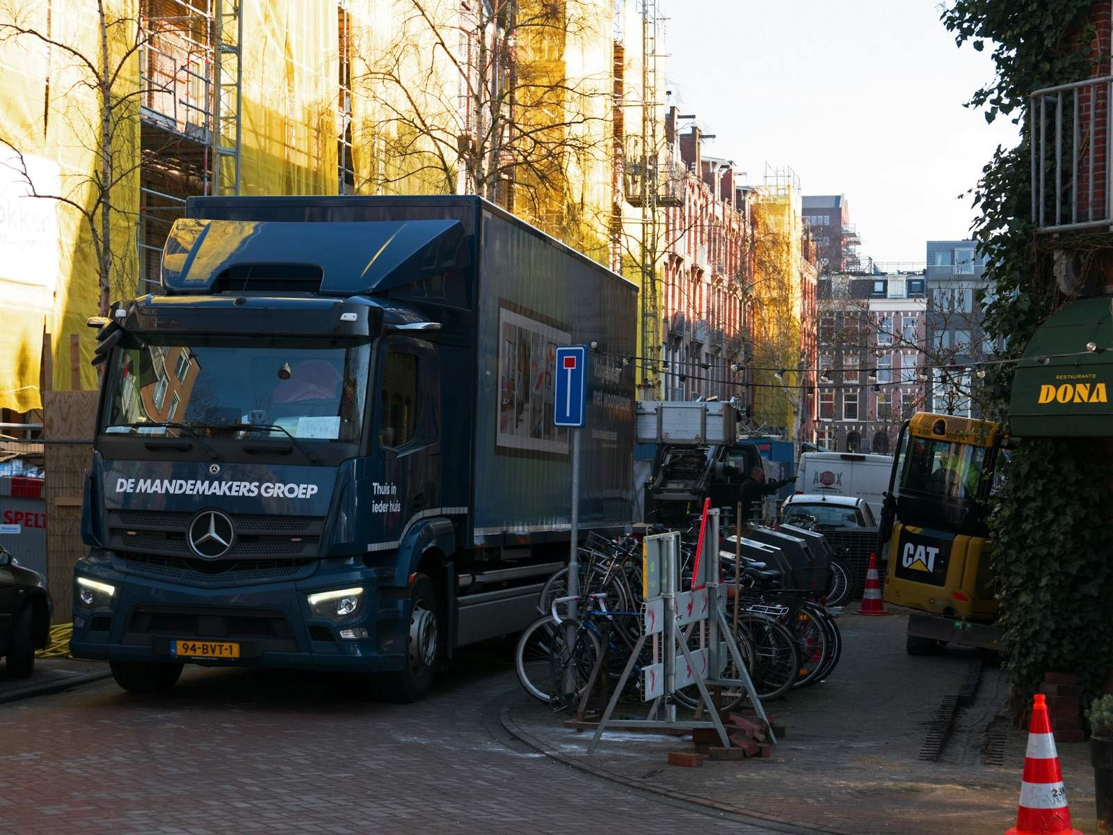 Een vrachtwagen geparkeerd in een smalle straat in de Kinkerbuurt in Amsterdam, naast fietsen en een parkeerbord